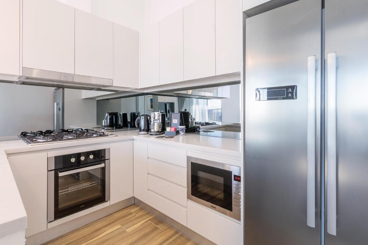 Meriton Suites Bondi Junction Сидней Экстерьер фото The photo shows a modern kitchen with a clean and minimalist design. It features white cabinetry and a stainless steel refrigerator. The kitchen includes a gas stove with an oven below it, as well as a microwave. There are several kitchen appliances,