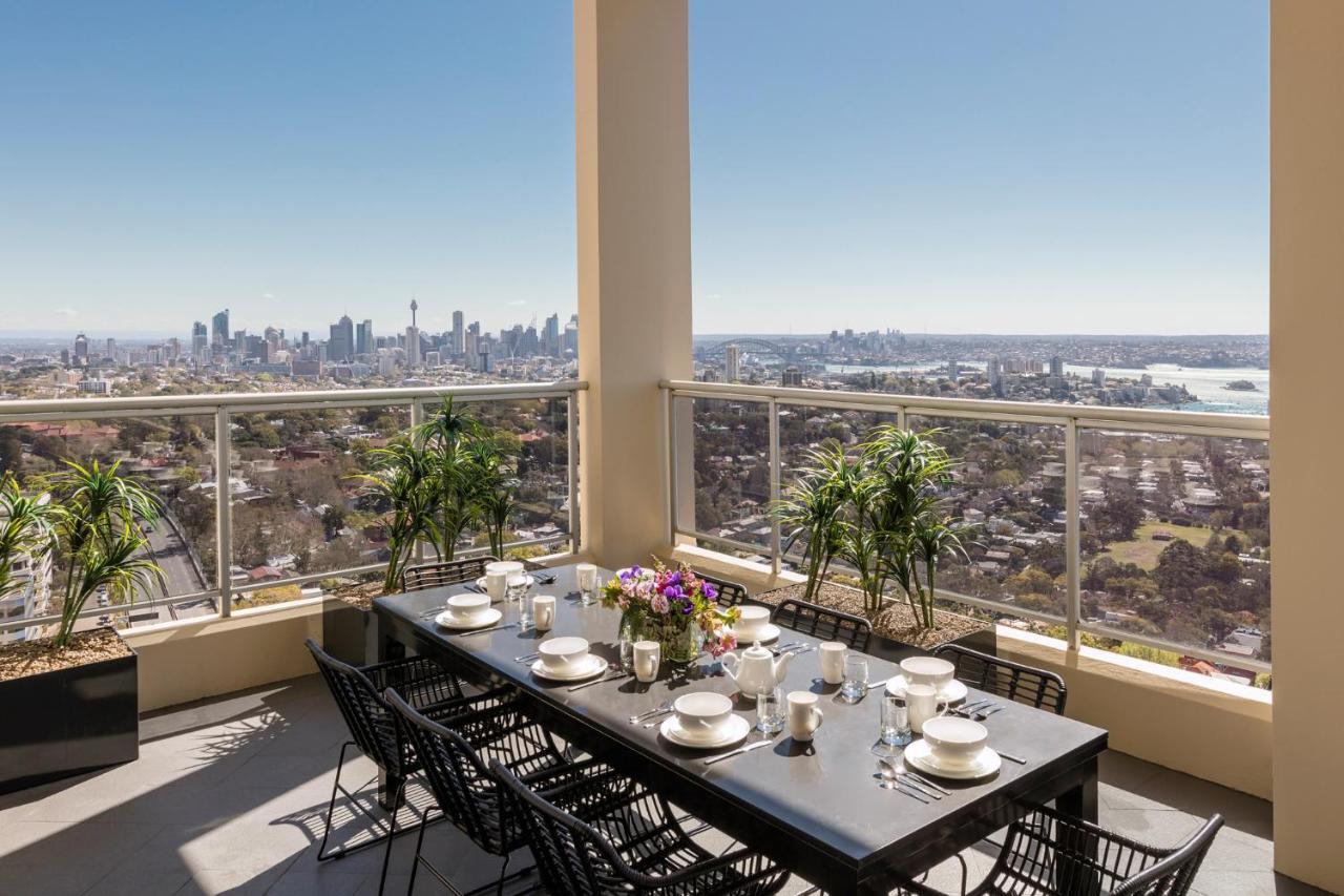 Meriton Suites Bondi Junction Сидней Экстерьер фото The photo shows a beautifully arranged outdoor dining area on a balcony. There is a long black dining table set for a meal, with plates, glasses, and decorative items like a vase of flowers. Surrounding the table are stylish black chairs. In the back
