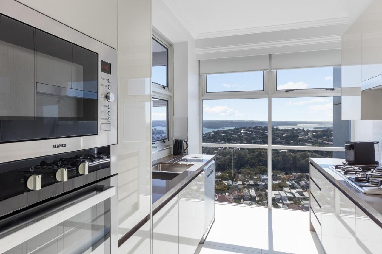 Meriton Suites Bondi Junction Сидней Экстерьер фото The photo shows a modern kitchen with sleek, shiny white cabinets and a large window that offers a panoramic view of the outside landscape. The kitchen features built-in appliances, including an oven and a stove, with a stylish countertop. The spacio