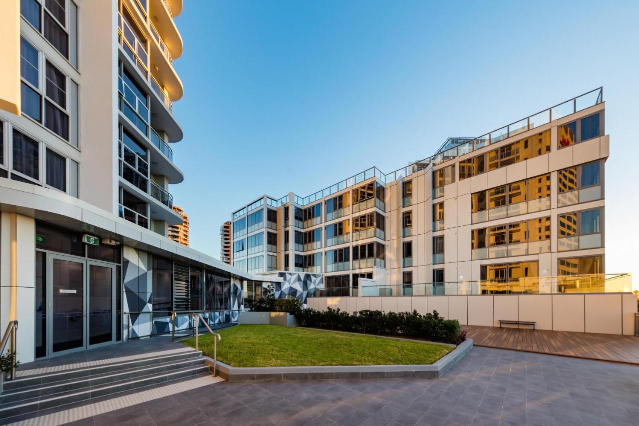 Meriton Suites Bondi Junction Сидней Экстерьер фото The photo showcases a modern residential area featuring contemporary buildings. In the foreground, there is a landscaped green space surrounded by well-designed architecture. The buildings have large glass windows, reflecting the light, and feature a