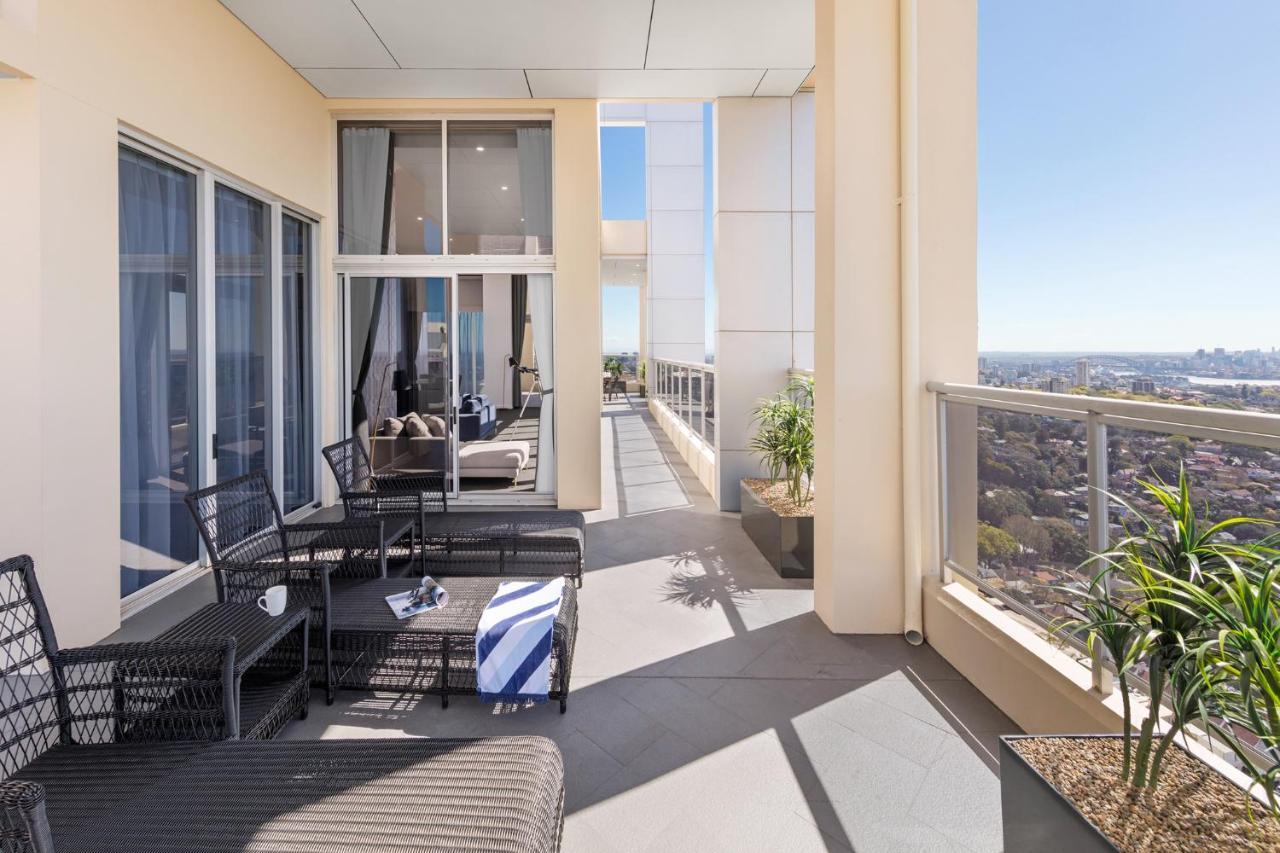 Meriton Suites Bondi Junction Сидней Экстерьер фото The photo shows a spacious balcony or terrace area of a high-rise building. It features modern outdoor furniture, including a seating arrangement with dark wicker chairs and a table. There are cushions, and a blue and white striped blanket is draped 