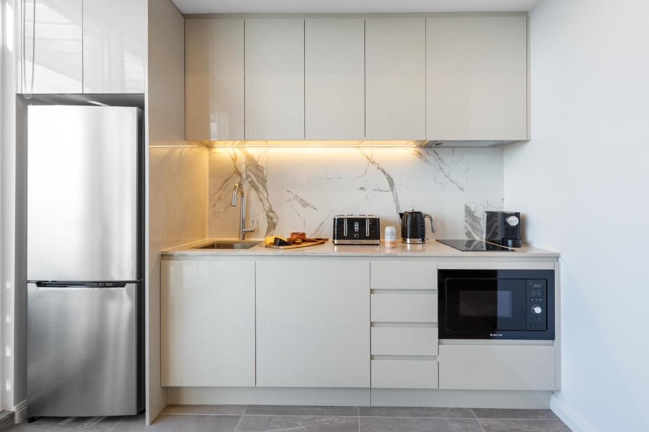 Meriton Suites Bondi Junction Сидней Экстерьер фото The photo shows a modern kitchen featuring a sleek design. It includes light-colored cabinetry with a smooth finish and upper cabinets that blend seamlessly with the wall. The countertop is made of a light stone, complementing the overall aesthetic. 
